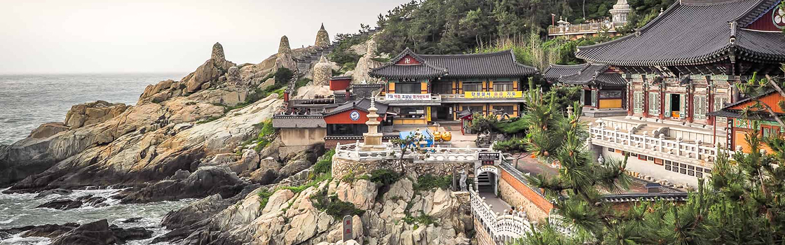 Templo Haedong Yonggungsa, que fica no meio de montanha de pedras, com árvores e envolto do mar